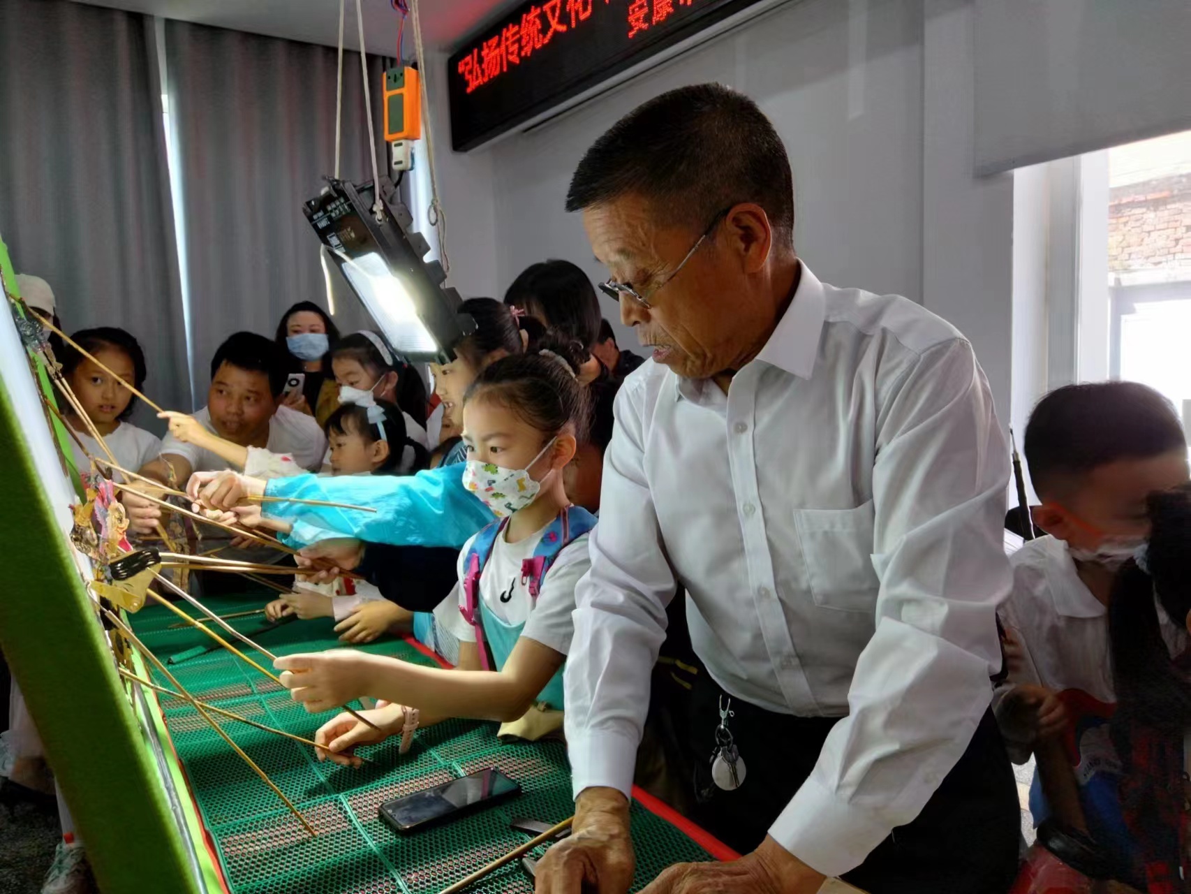 5月28日,市图书馆举办道情皮影戏展演。图为活动中,老艺人让小朋友们也拿起了道具进行了一番体验。.jpg